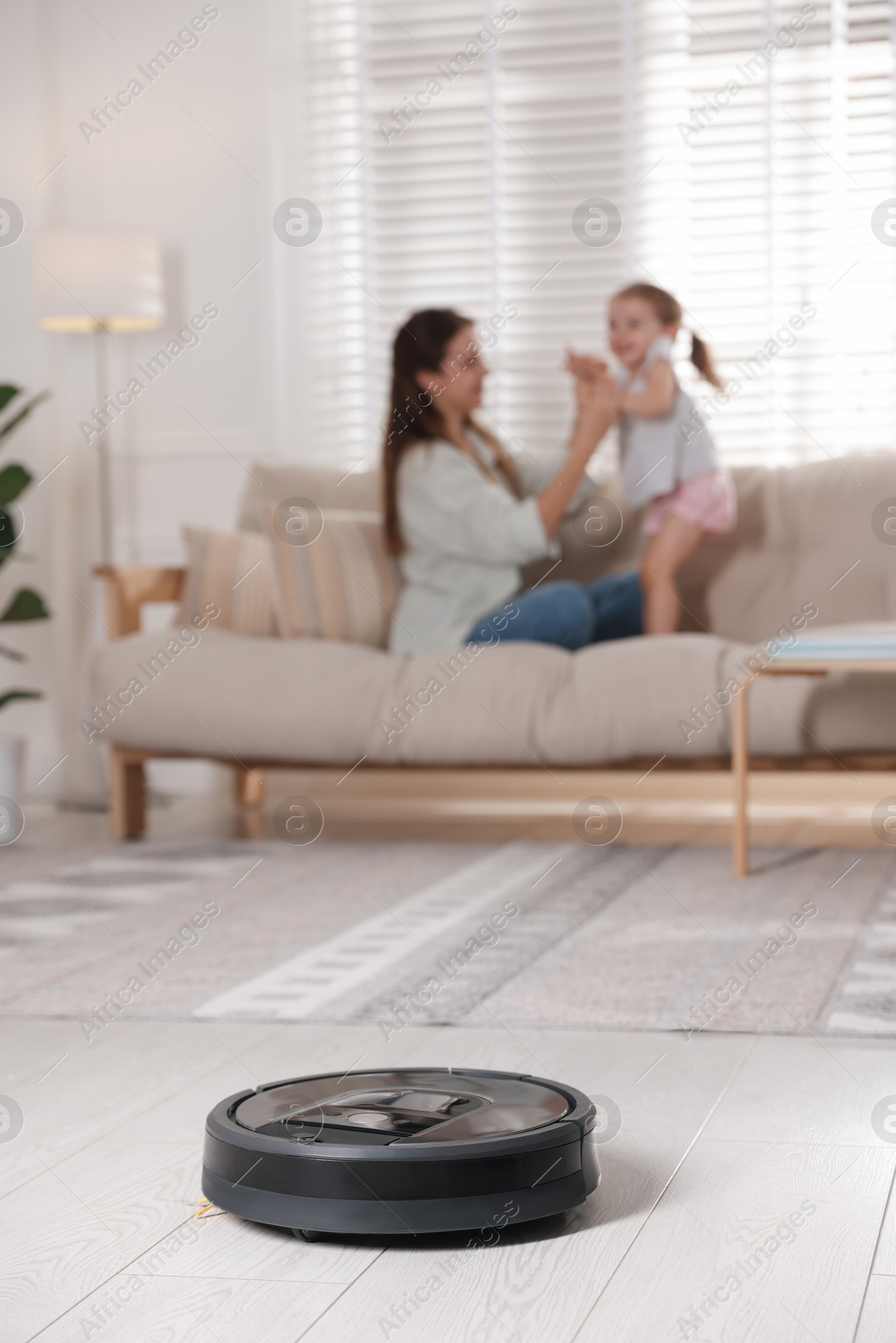 Photo of Mother spending time with her daughter in room, focus on robotic vacuum cleaner