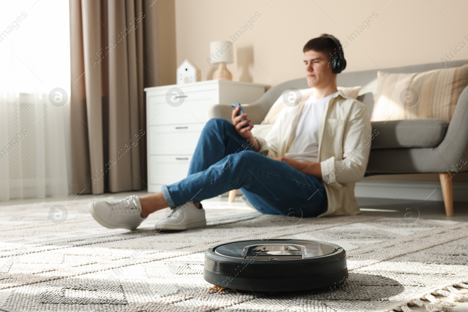 Photo of Robotic vacuum cleaner cleaning carpet while man relaxing at home