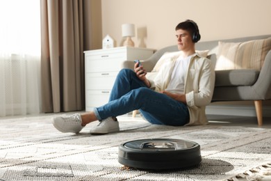 Photo of Robotic vacuum cleaner cleaning carpet while man relaxing at home