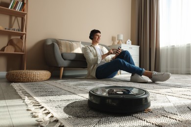 Photo of Robotic vacuum cleaner cleaning carpet while man relaxing at home