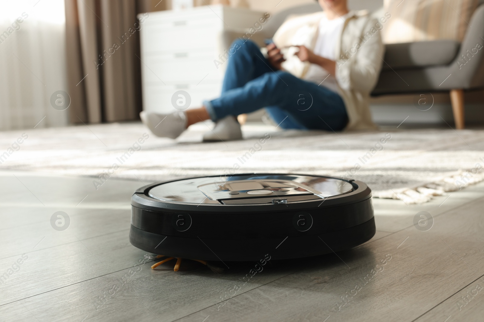 Photo of Robotic vacuum cleaner cleaning floor while man relaxing at home, selective focus