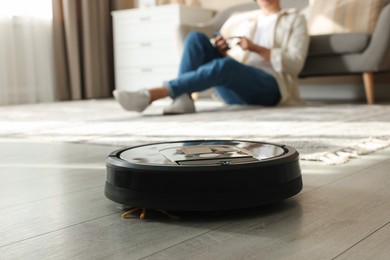 Photo of Robotic vacuum cleaner cleaning floor while man relaxing at home, selective focus