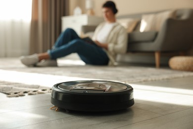 Photo of Robotic vacuum cleaner cleaning floor while man relaxing at home, selective focus