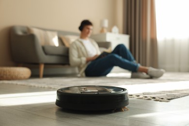 Photo of Robotic vacuum cleaner cleaning floor while man relaxing at home, selective focus