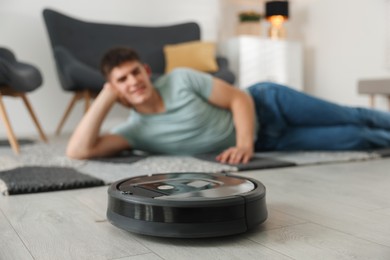 Photo of Robotic vacuum cleaner cleaning floor while man relaxing at home, selective focus