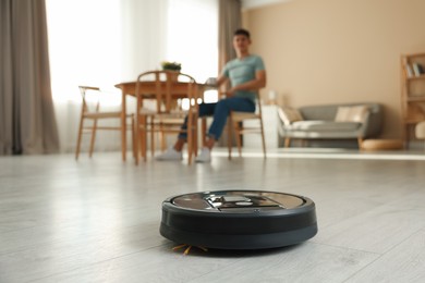 Photo of Robotic vacuum cleaner cleaning floor while man relaxing at home, selective focus