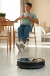 Photo of Robotic vacuum cleaner cleaning floor while man relaxing at home, selective focus