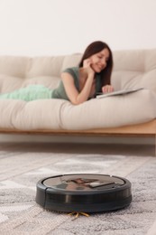 Photo of Young woman resting at home, focus on robotic vacuum cleaner