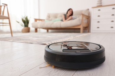 Photo of Young woman resting at home, focus on robotic vacuum cleaner