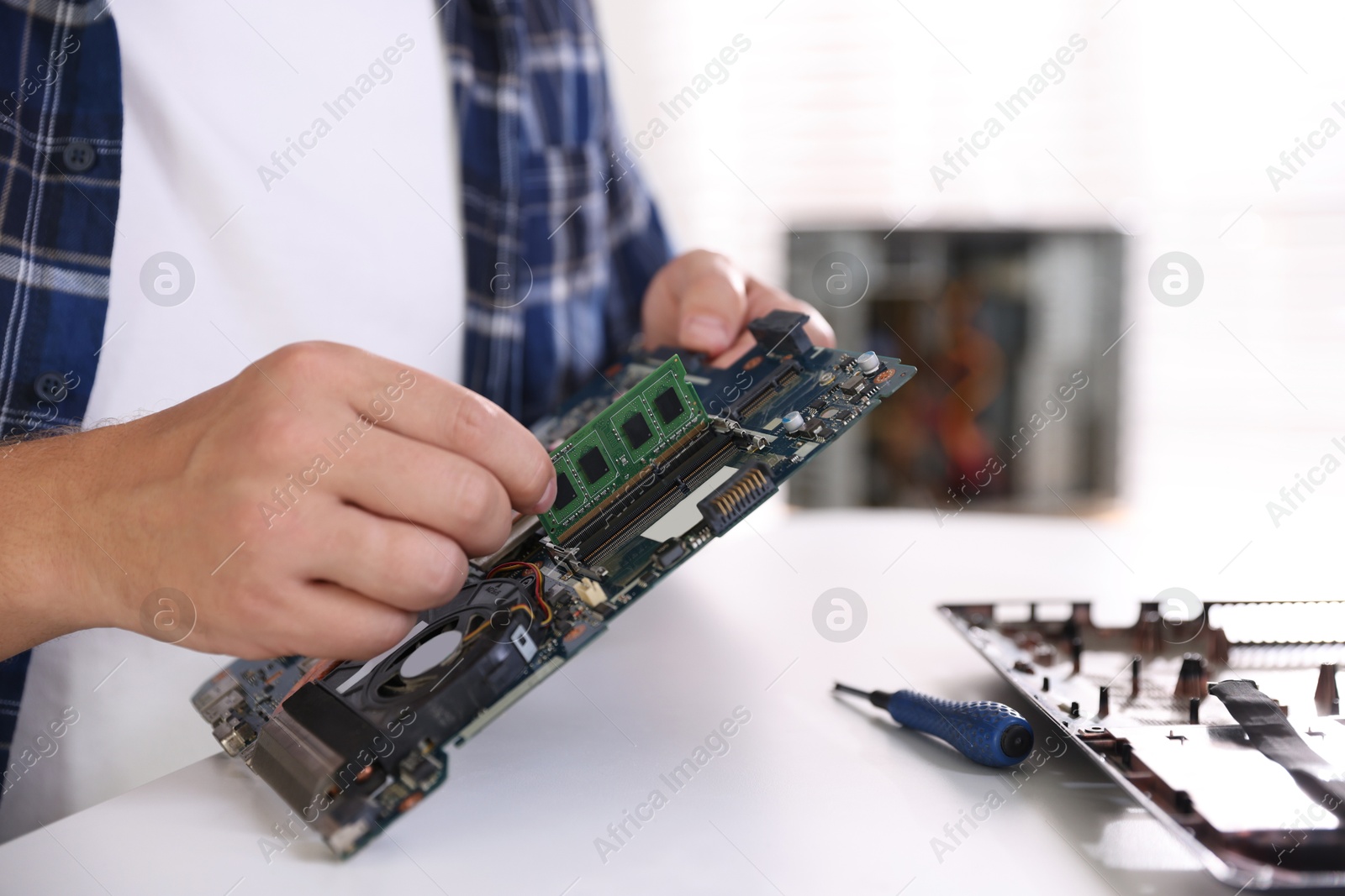 Photo of Man installing computer chip onto motherboard at white table, closeup