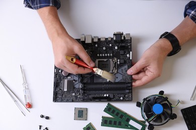 Photo of Man installing computer chip onto motherboard at white table, top view