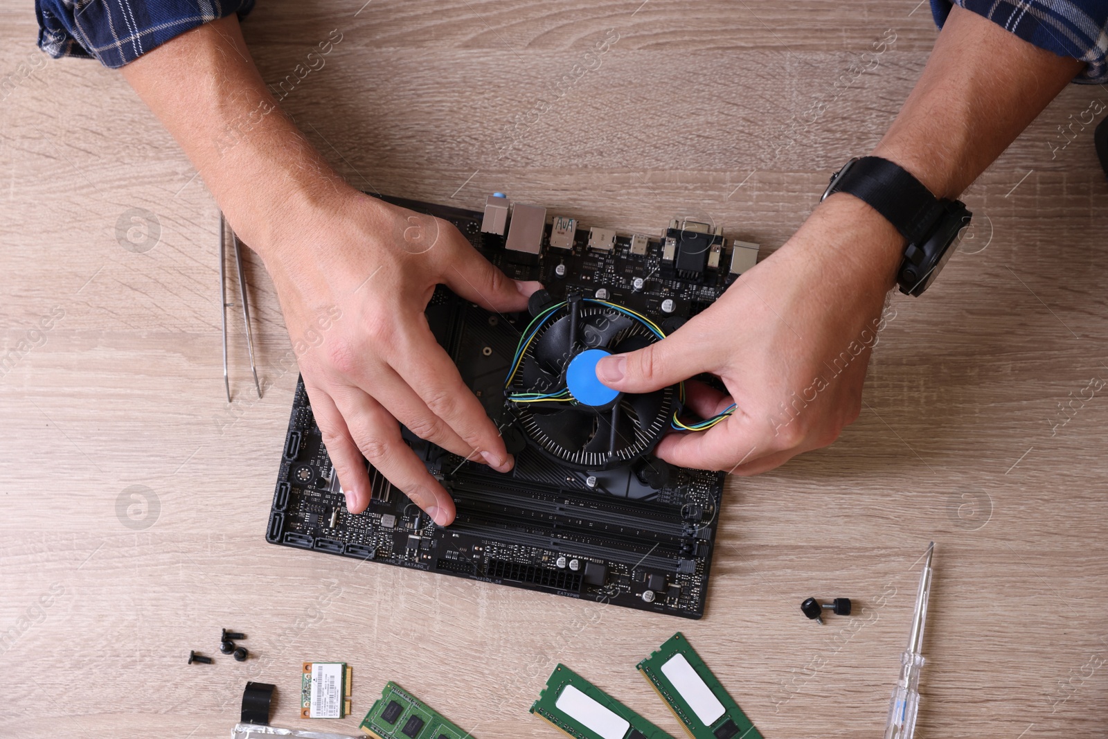 Photo of Man installing computer chip onto motherboard at wooden table, top view