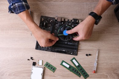 Photo of Man installing computer chip onto motherboard at wooden table, top view