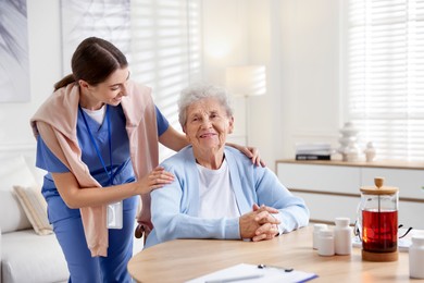 Photo of Caregiver supporting senior woman indoors. Home health care service