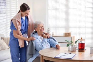 Photo of Caregiver covering senior woman with blanket indoors. Home health care service