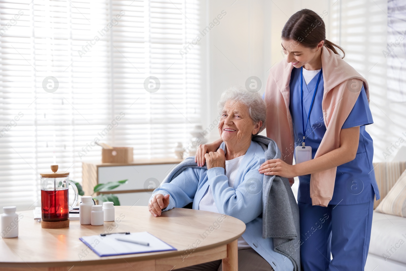 Photo of Caregiver covering senior woman with blanket indoors. Home health care service