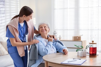 Photo of Caregiver covering senior woman with blanket indoors. Home health care service