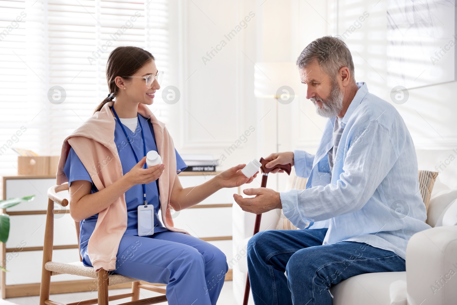 Photo of Caregiver giving pills to senior man indoors. Home health care service