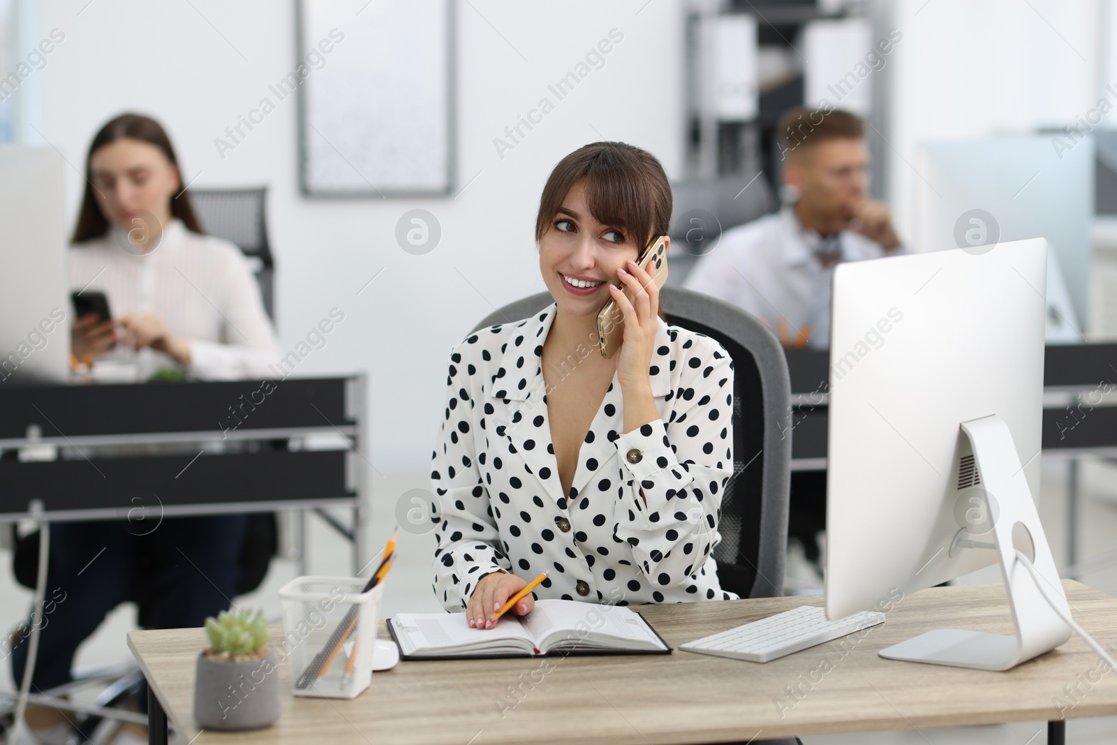 Photo of Saleswoman making notes while talking on phone at desk in office