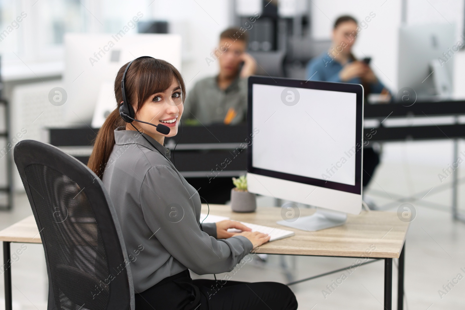 Photo of Saleswoman talking to client via headset at desk in office