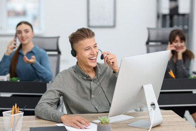 Photo of Salesman talking to client via headset at desk in office