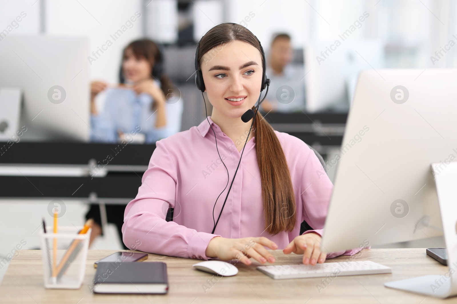 Photo of Saleswoman talking to client via headset at desk in office