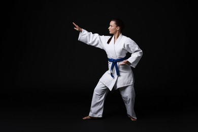 Photo of Young woman in kimono practicing karate on black background