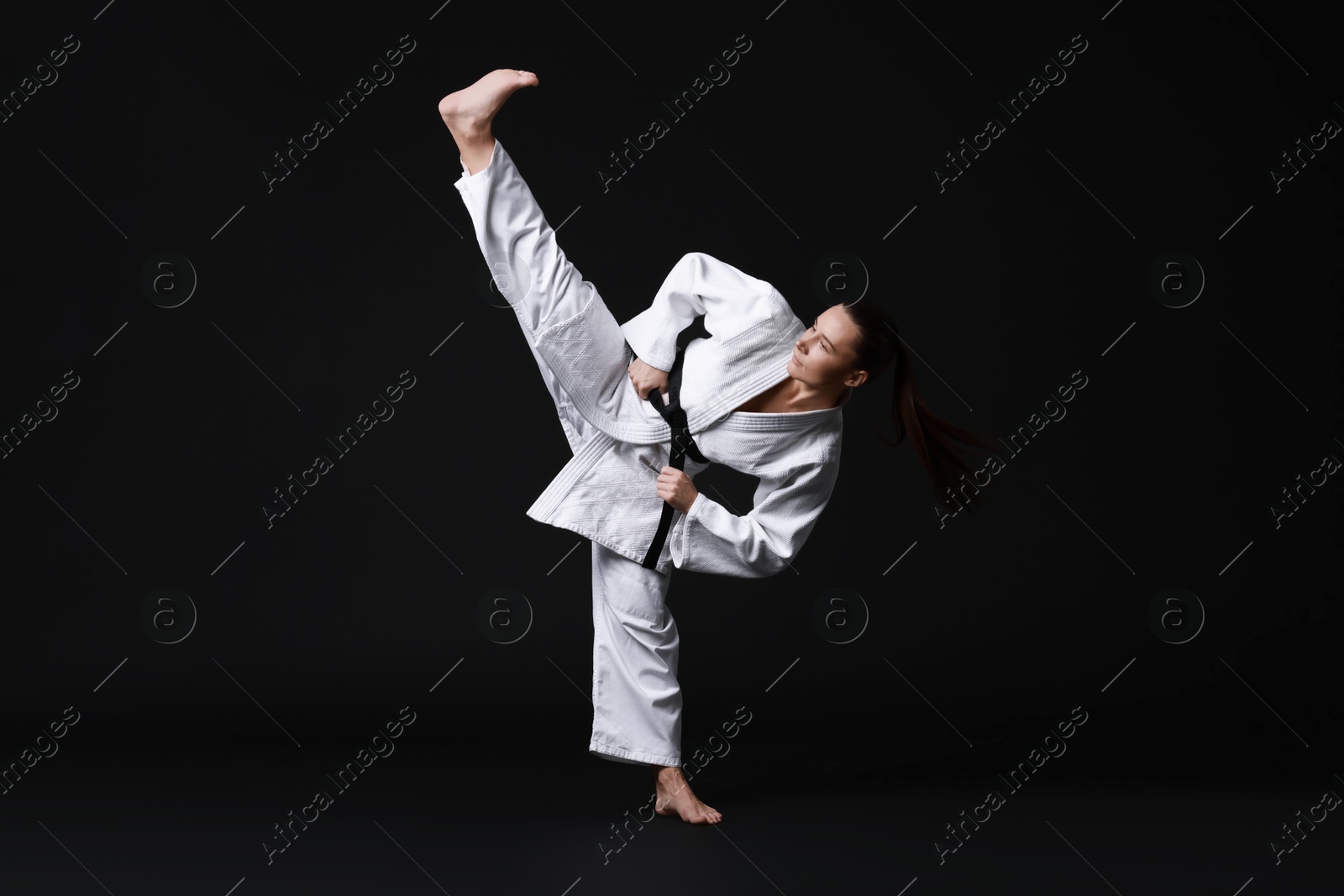 Photo of Young woman in kimono practicing karate on black background