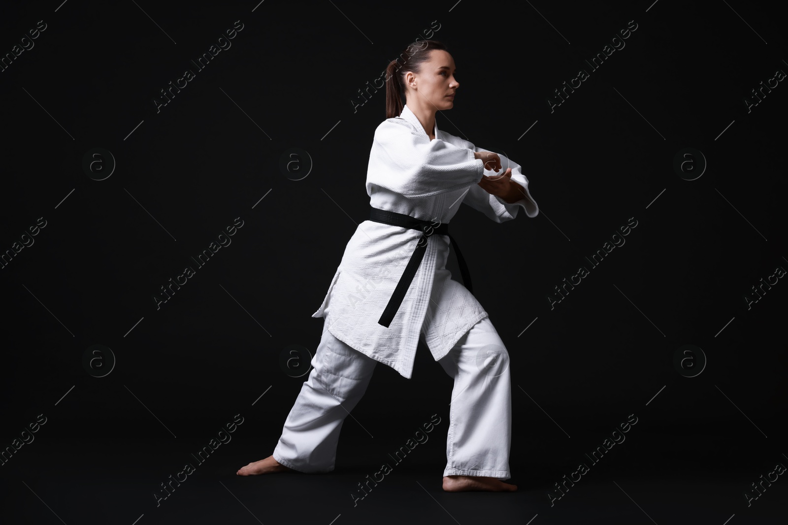 Photo of Young woman in kimono practicing karate on black background