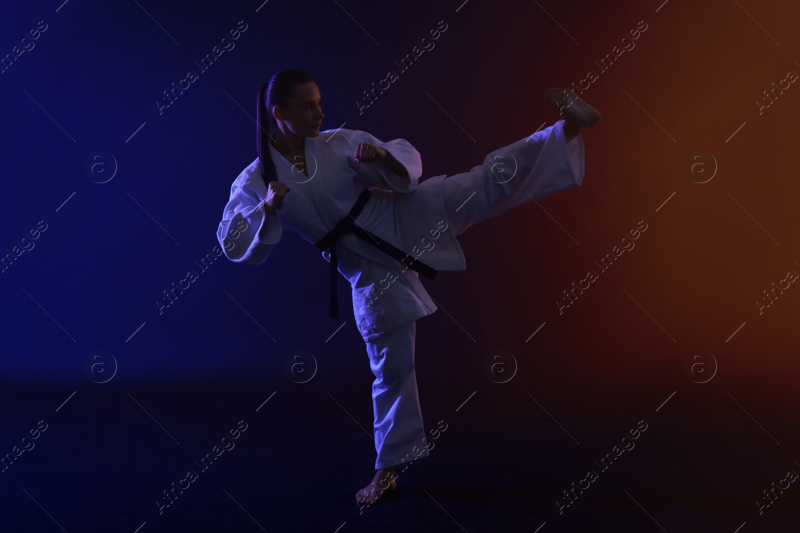 Photo of Young woman in kimono practicing karate on dark background