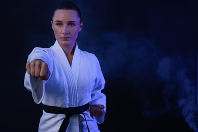 Photo of Karate fighter in kimono and smoke on dark background, space for text