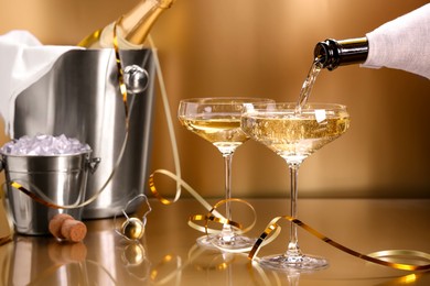 Photo of Pouring champagne into glass against golden background, closeup