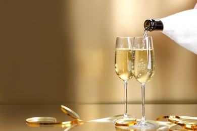 Photo of Pouring champagne into glass against golden background, closeup. Space for text