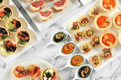 Photo of Many different tasty canapes on white marble table, flat lay