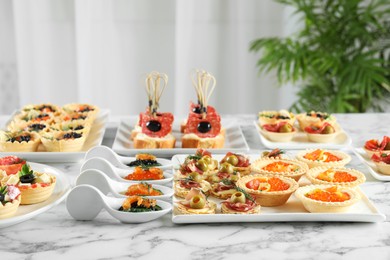 Photo of Many different tasty canapes on white marble table