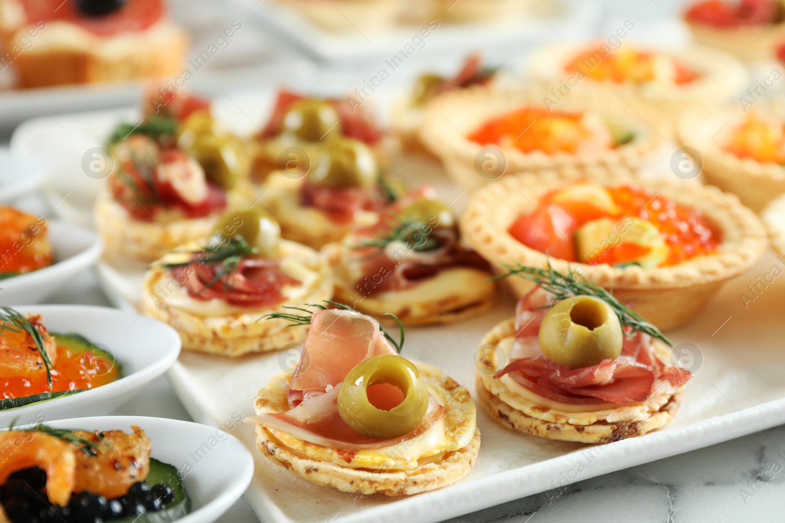 Photo of Many different tasty canapes on white marble table, closeup