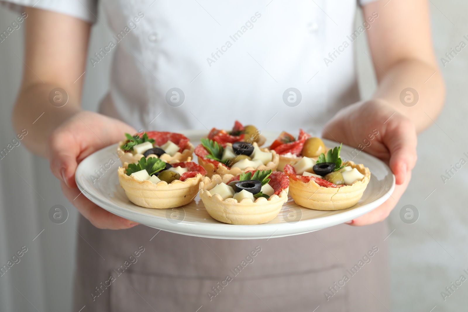 Photo of Woman holding plate with tasty canapes on light grey background, closeup