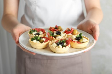 Photo of Woman holding plate with tasty canapes on light grey background, closeup