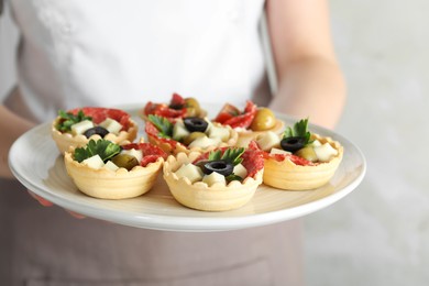 Photo of Woman holding plate with tasty canapes on light grey background, closeup