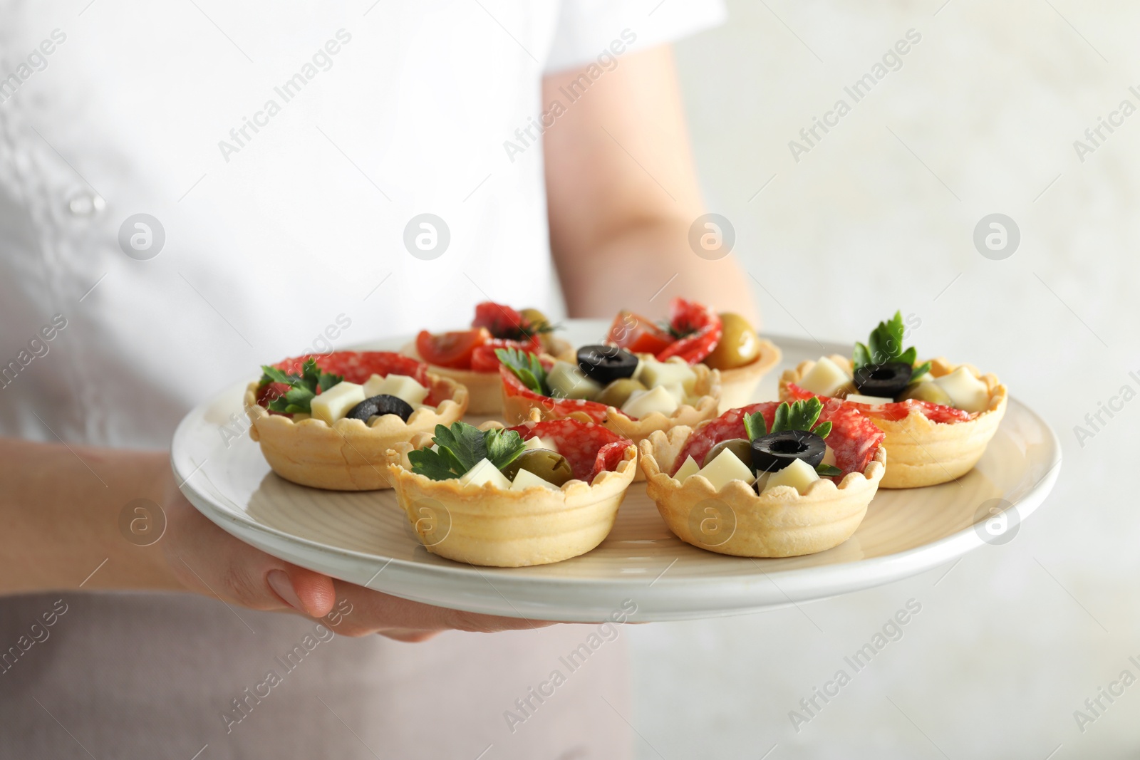 Photo of Woman holding plate with tasty canapes on light grey background, closeup