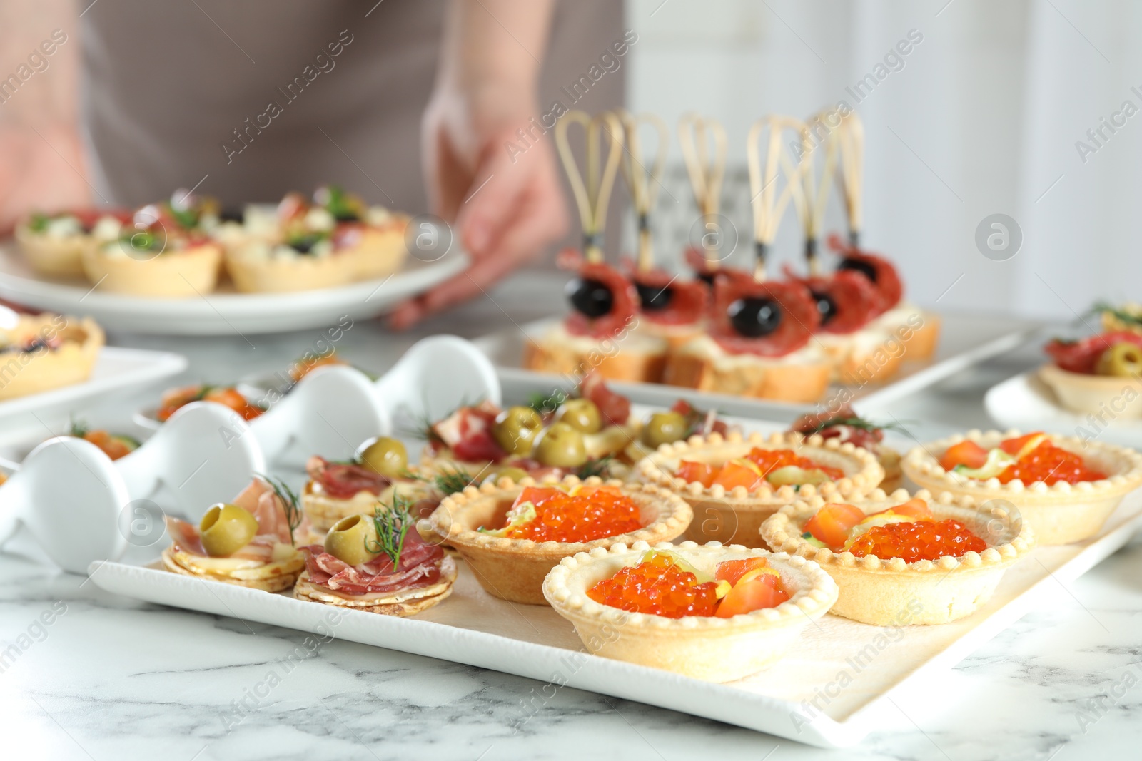 Photo of Woman with many different tasty canapes at white marble table, closeup