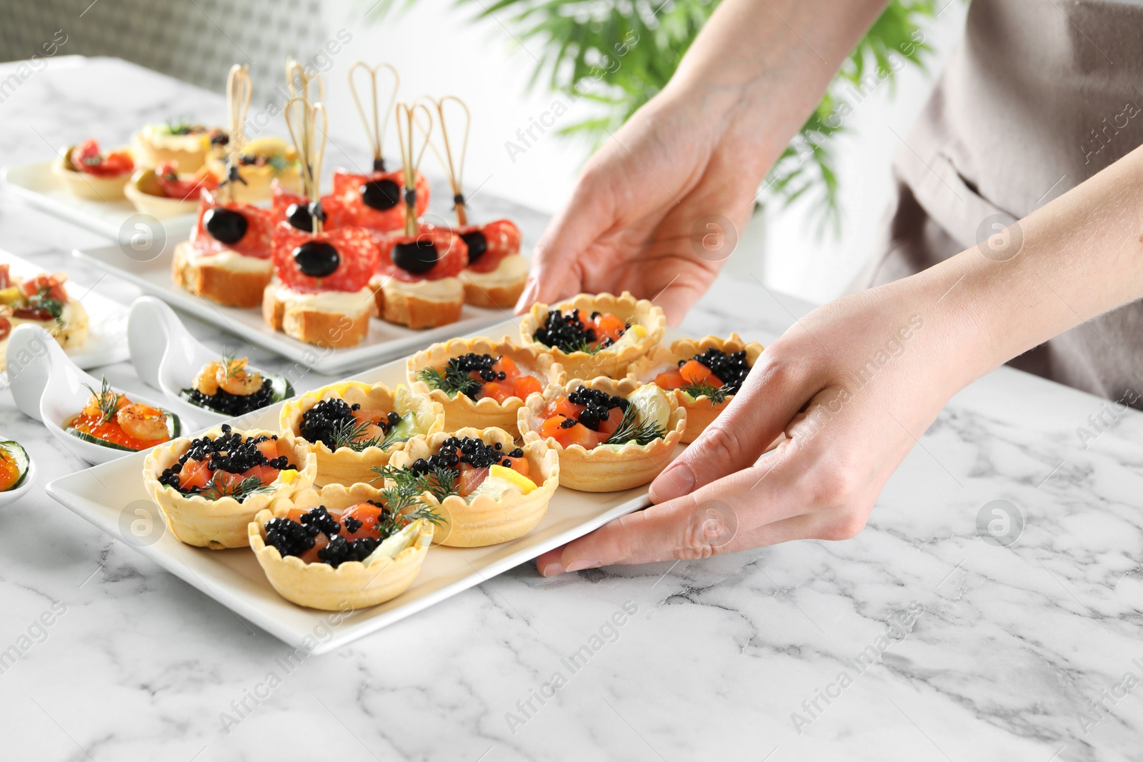 Photo of Woman with many different tasty canapes at white marble table, closeup