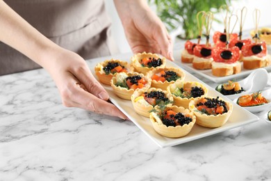 Photo of Woman with many different tasty canapes at white marble table, closeup