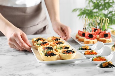 Photo of Woman with many different tasty canapes at white marble table, closeup