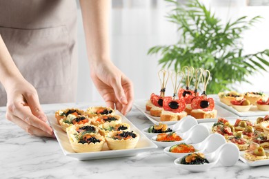 Photo of Woman with many different tasty canapes at white marble table, closeup