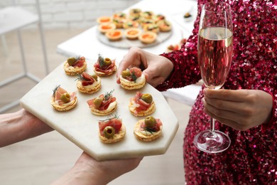 Photo of Woman taking tasty canape from waiter with board indoors, closeup