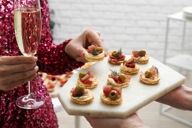 Photo of Woman taking tasty canape from waiter with board indoors, closeup