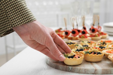 Photo of Woman taking tasty canape at white wooden table, closeup