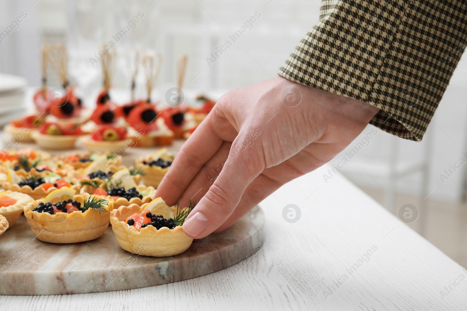 Photo of Woman taking tasty canape at white wooden table, closeup