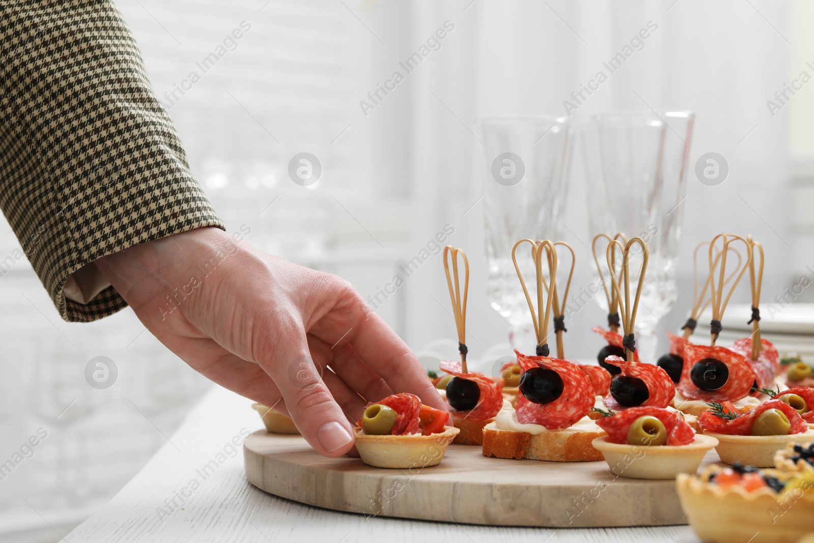 Photo of Woman taking tasty canape at white wooden table, closeup